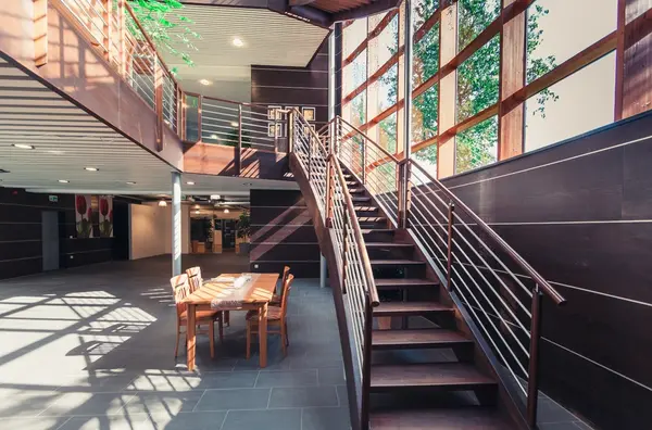 Modernes, lichtdurchflutetes Treppenhaus mit großen Fenstern und einem Holztisch im Foyer.