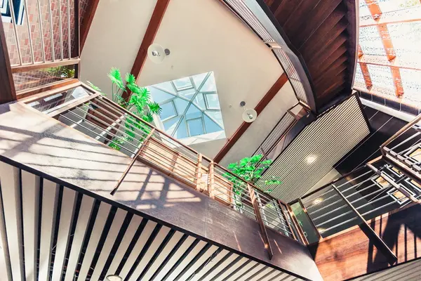 Modernes Atrium mit Glasdach, Holzelementen und grünen Pflanzen im Innenbereich.