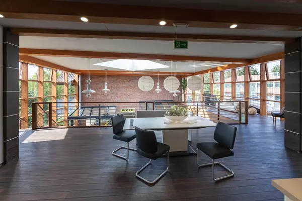 Moderner, heller Büroraum mit großen Fenstern, Holzboden und stilvollen Möbeln.